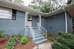 A two-story house with a front porch, a staircase, and a garden with flowers and shrubs.