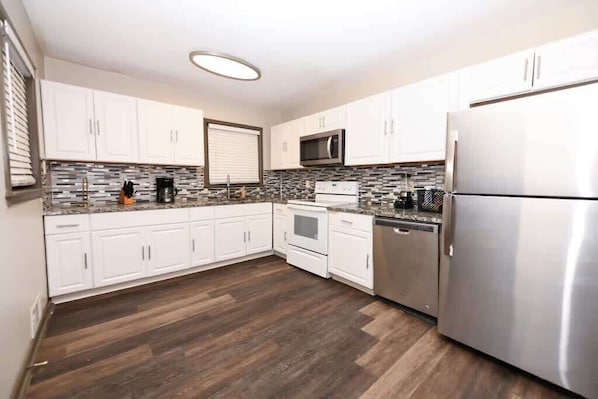 A modern kitchen with white cabinets, a stainless steel refrigerator, a microwave, and a tiled backsplash.