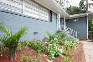 A residential building with a blue exterior, a covered porch, and a small garden with various plants and flowers.