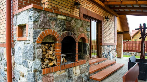 A stone building with two brick ovens, steps leading to a covered patio area, and outdoor seating.