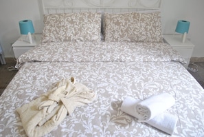 A neatly made bed with a patterned bedspread, two pillows, and a rolled towel on the bed.