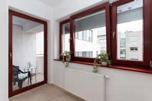 Una habitación con una puerta corrediza de vidrio que da a un balcón, un radiador blanco y dos ventanas con plantas en los alféizares.