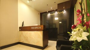 A reception desk with a marble top and a wooden base, a sign above it, and a potted plant with flowers to the right. - VIP Apartments Oławska (Wroclaw)