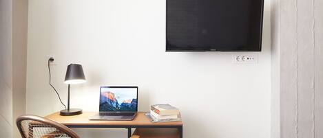 Un espacio de trabajo con escritorio, ordenador portátil, libros y televisión montada en la pared.