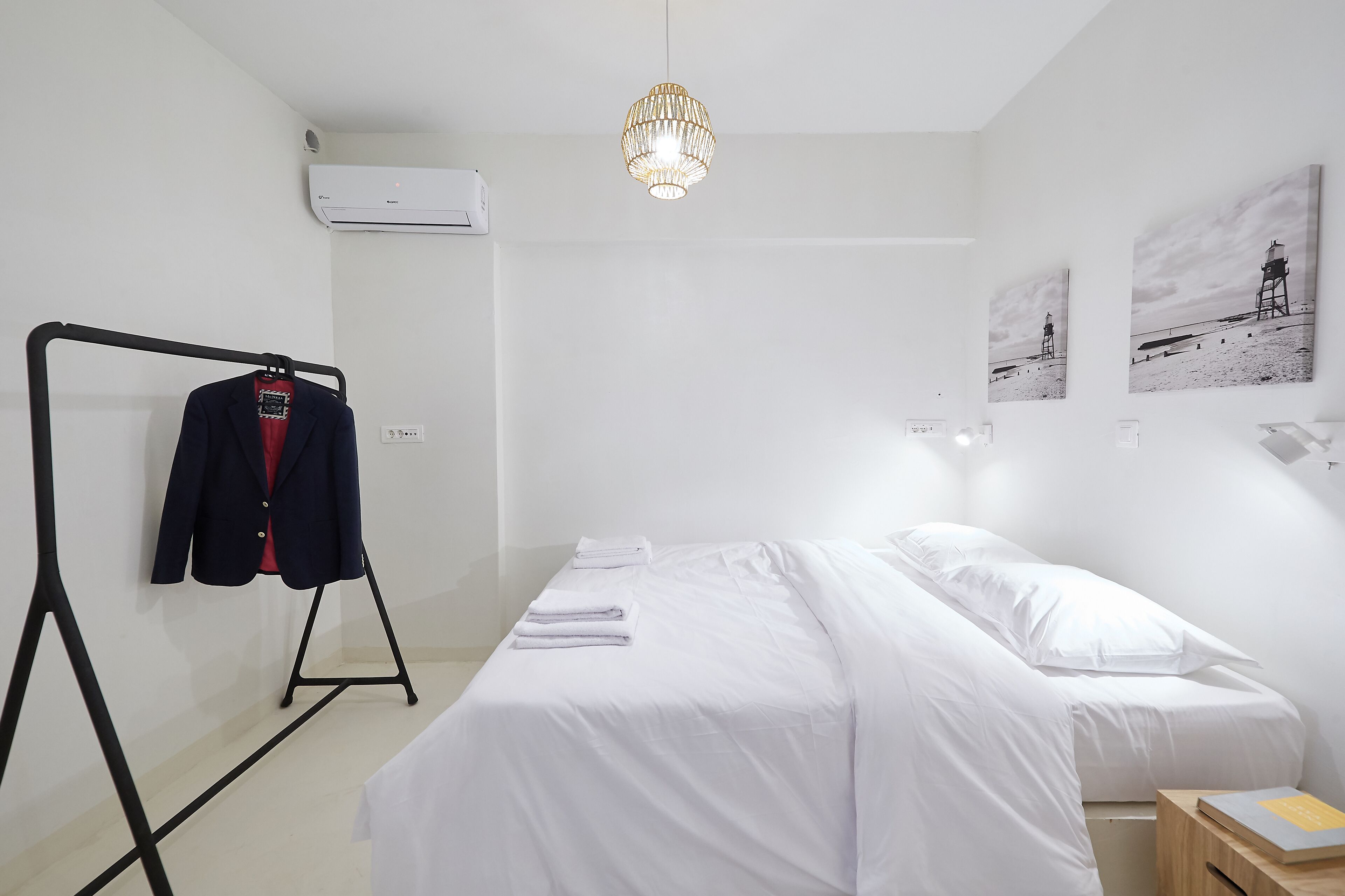 A minimalist hotel room with a bed, a hanging coat rack, and a pendant light.