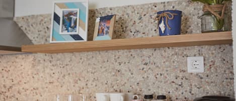 A kitchen shelf with various mugs, a picture frame, and a vase with flowers.