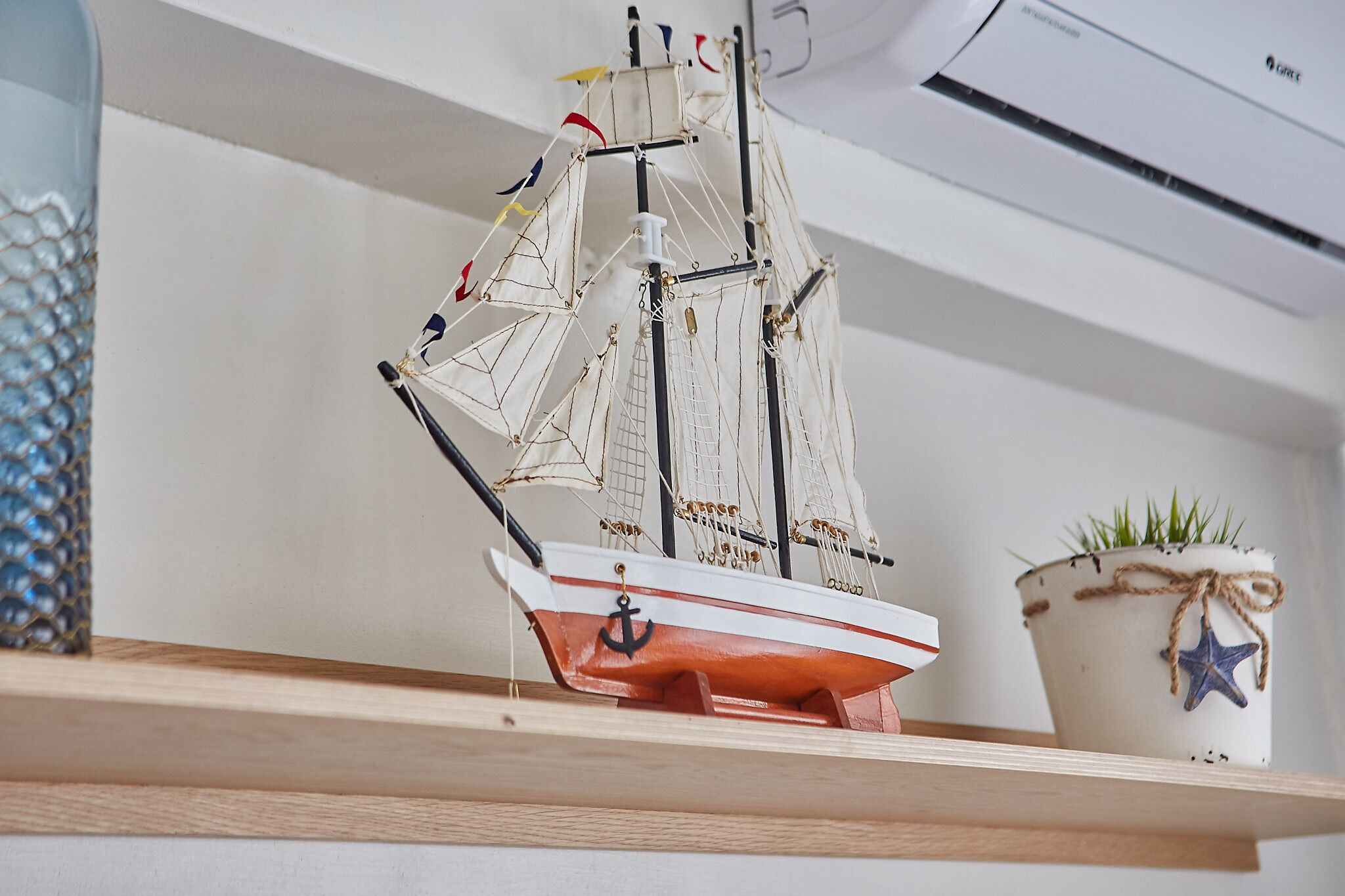 A model ship on a shelf, a potted plant with a star decoration, and a wall-mounted air conditioner.