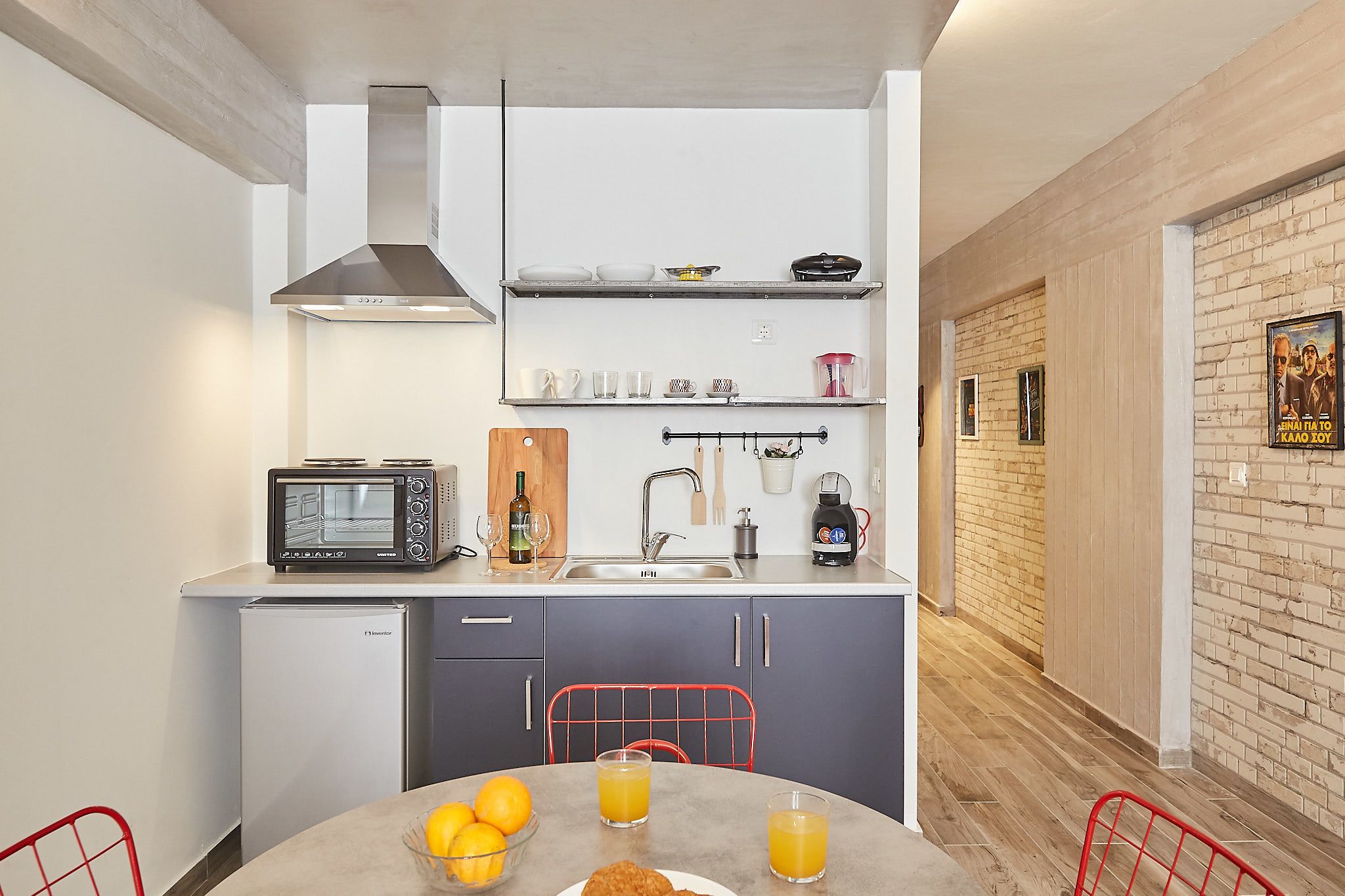 A compact kitchen with a microwave, toaster, and coffee maker on the counter, a small refrigerator, and a dining table with breakfast items.