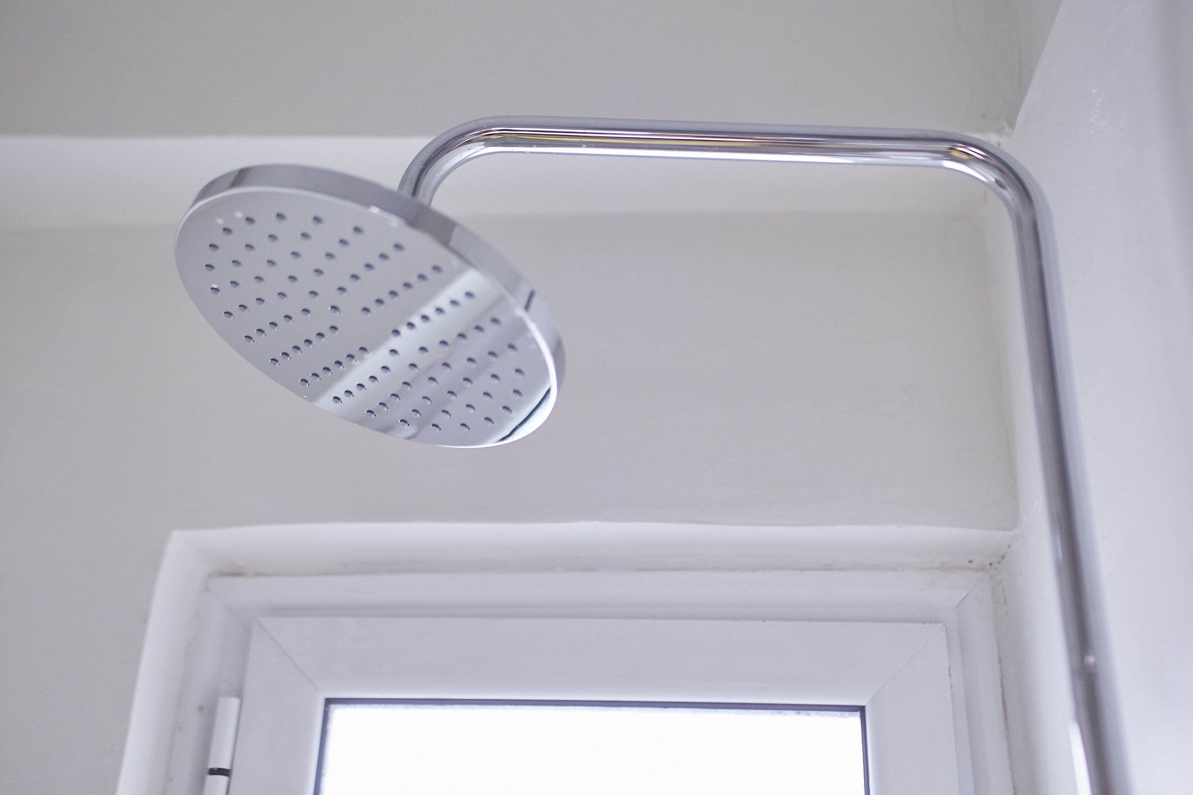 A showerhead in a bathroom with a white wall and a door.