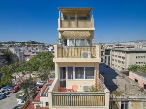 A multi-story building with balconies, a parking area, and a view of the cityscape.