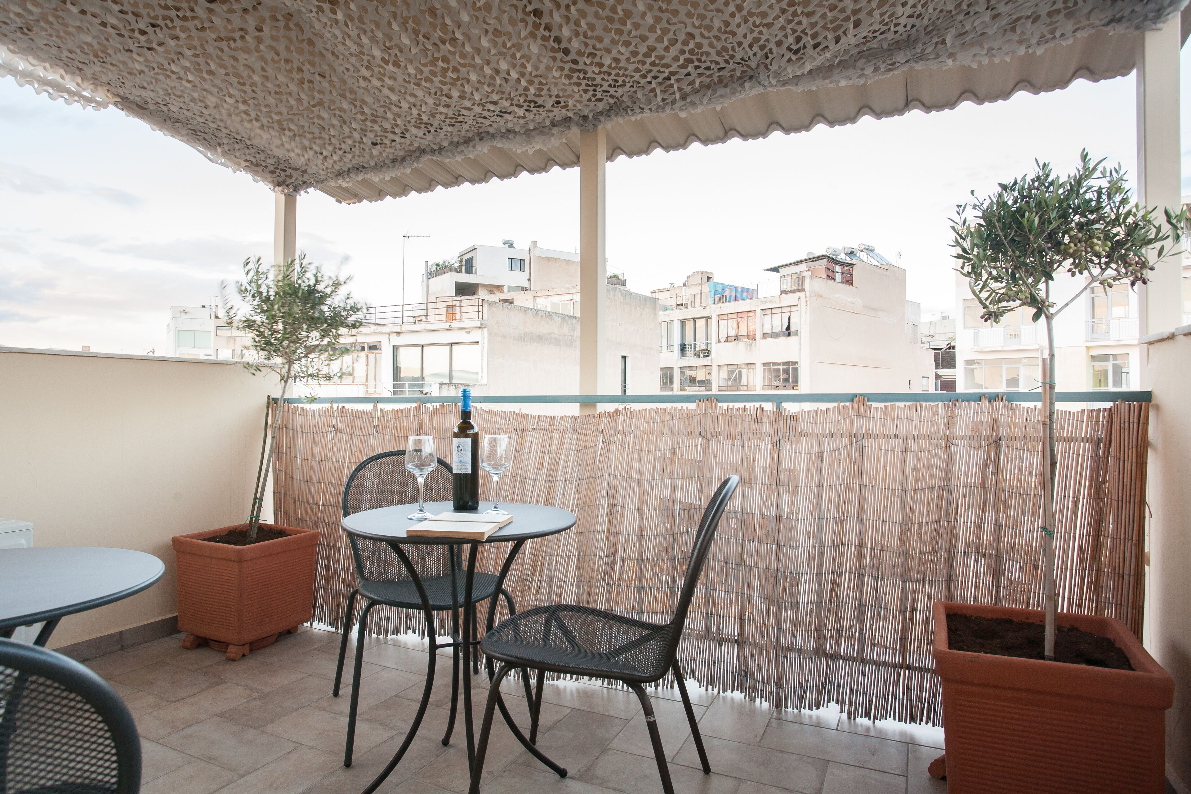Un área de estar al aire libre cubierta con dos mesas, sillas, una botella de vino y dos macetas.