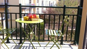 Un balcon avec une table et des chaises, une vue sur des immeubles et un arbre en arrière-plan.
