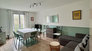 Un salon comprenant un coin repas, un canapé, un téléviseur et un mur orné d’une inscription disant « Bonjour, soleil ».