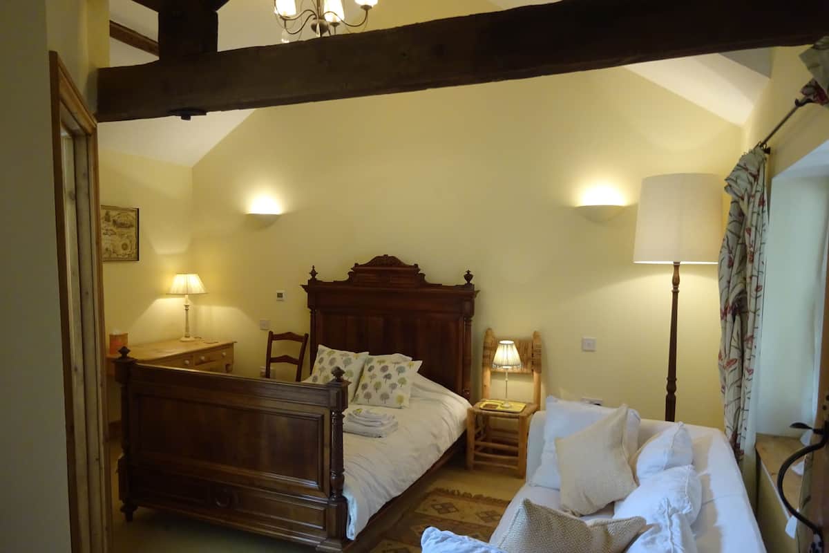 Ein Schlafzimmer mit einem Holzbett, einem Nachttisch mit Lampe, einem Sessel und einer Stehlampe.