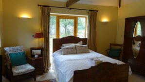 Ein Schlafzimmer mit einem hölzernen Bett, einem Sessel mit Kissen, einem Nachttisch mit Lampe und einem Fenster mit Vorhängen.