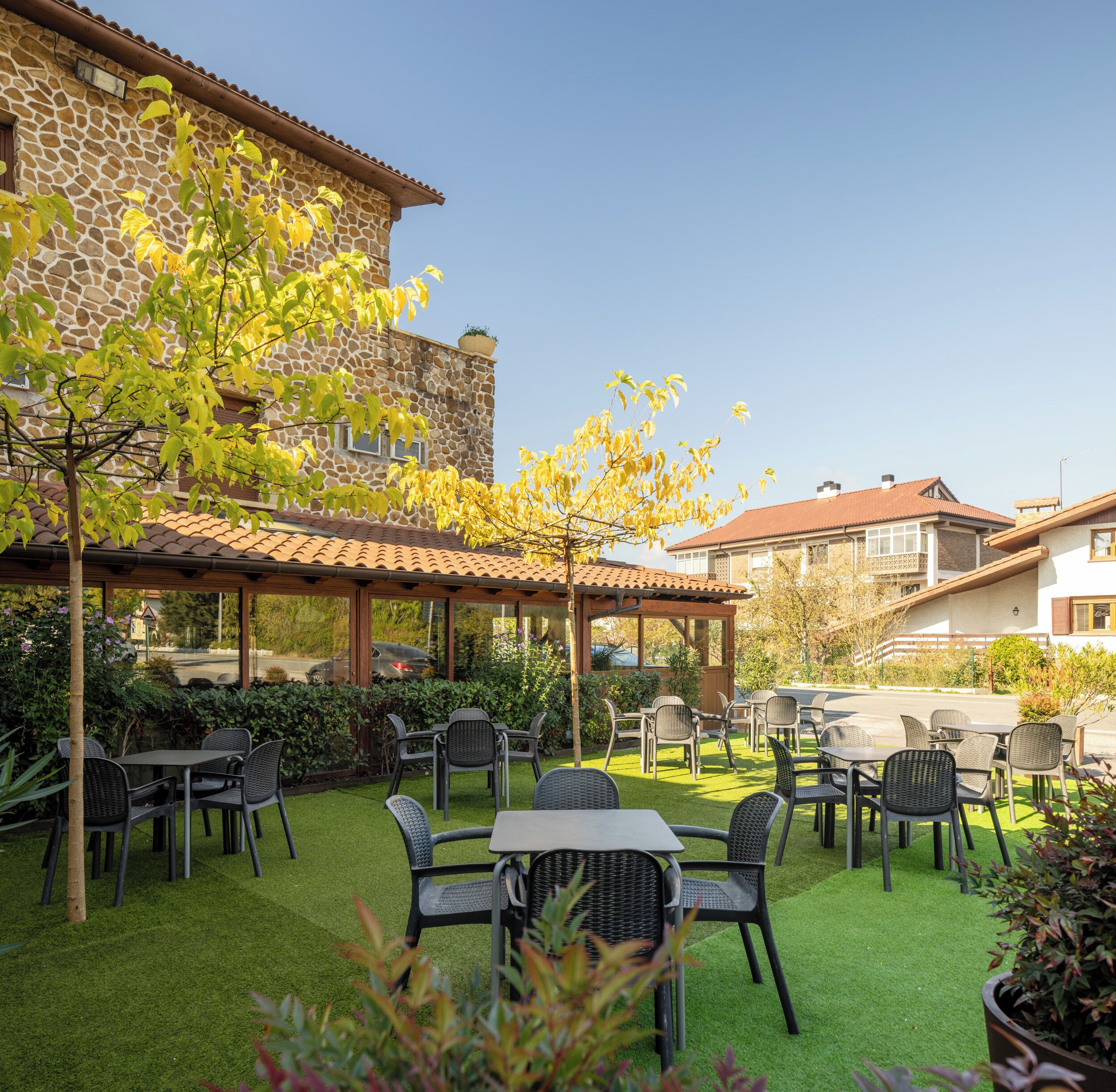An outdoor patio with tables and chairs, surrounded by stone buildings and greenery.