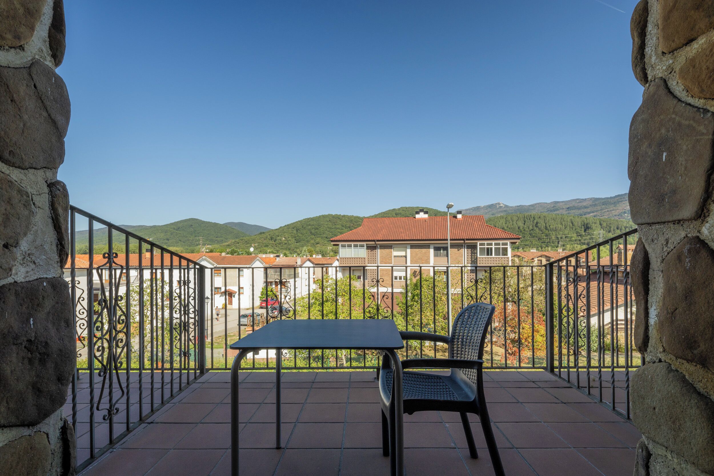Ein Balkon mit Tisch und Stuhl, der Blick auf eine Wohngegend mit Häusern und Hügeln freigibt.