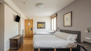 Una habitación de hotel con dos camas, televisión, un armario de madera y obras de arte en las paredes.