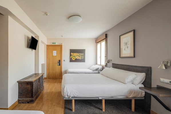 A hotel room with two beds, a TV, a wooden cabinet, and artwork on the walls. - Hostal Izar-Ondo (Arbizu)