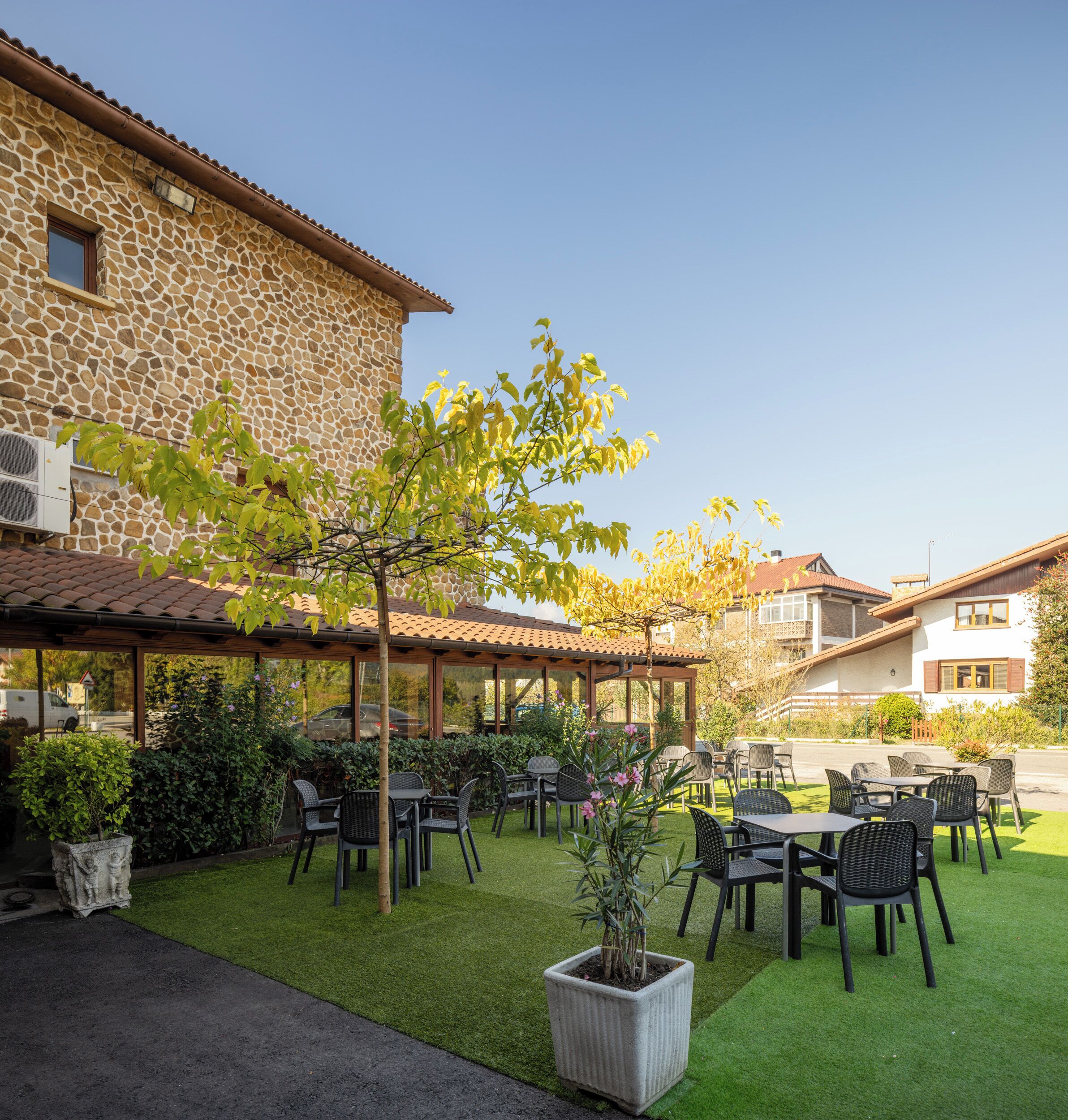 Un patio al aire libre con mesas y sillas, rodeado por un edificio de piedra con tejado de tejas.