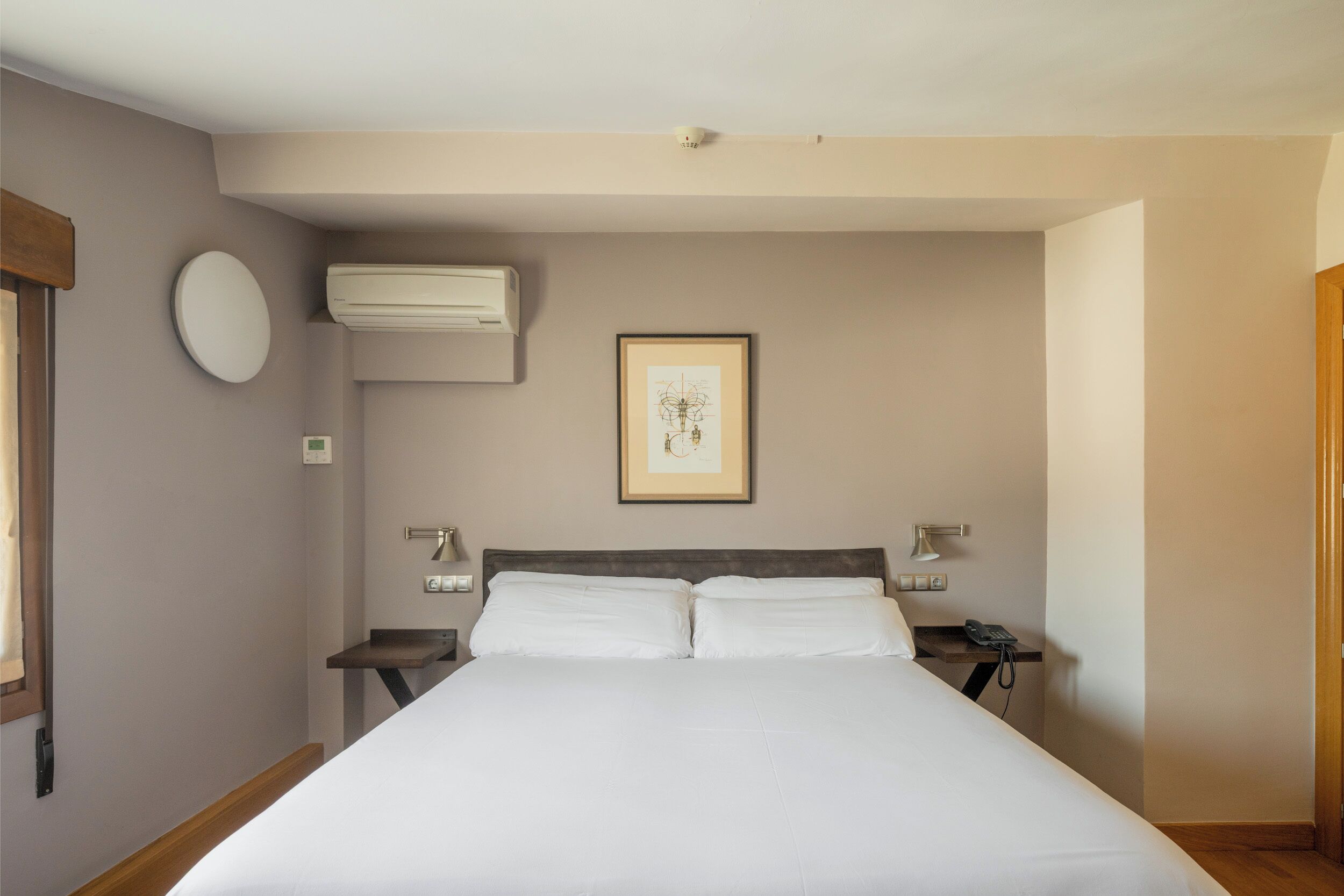 Habitación de hotel con una cama grande, mesitas de noche, aire acondicionado, una obra de arte enmarcada y un teléfono.