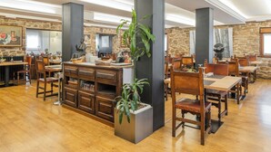 Un restaurante espacioso con mesas y sillas de madera, paredes de piedra y una columna central con una planta.