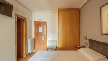 Een hotelkamer met een groot bed, een houten kledingkast, een stoel en een tafeltje met een lamp.