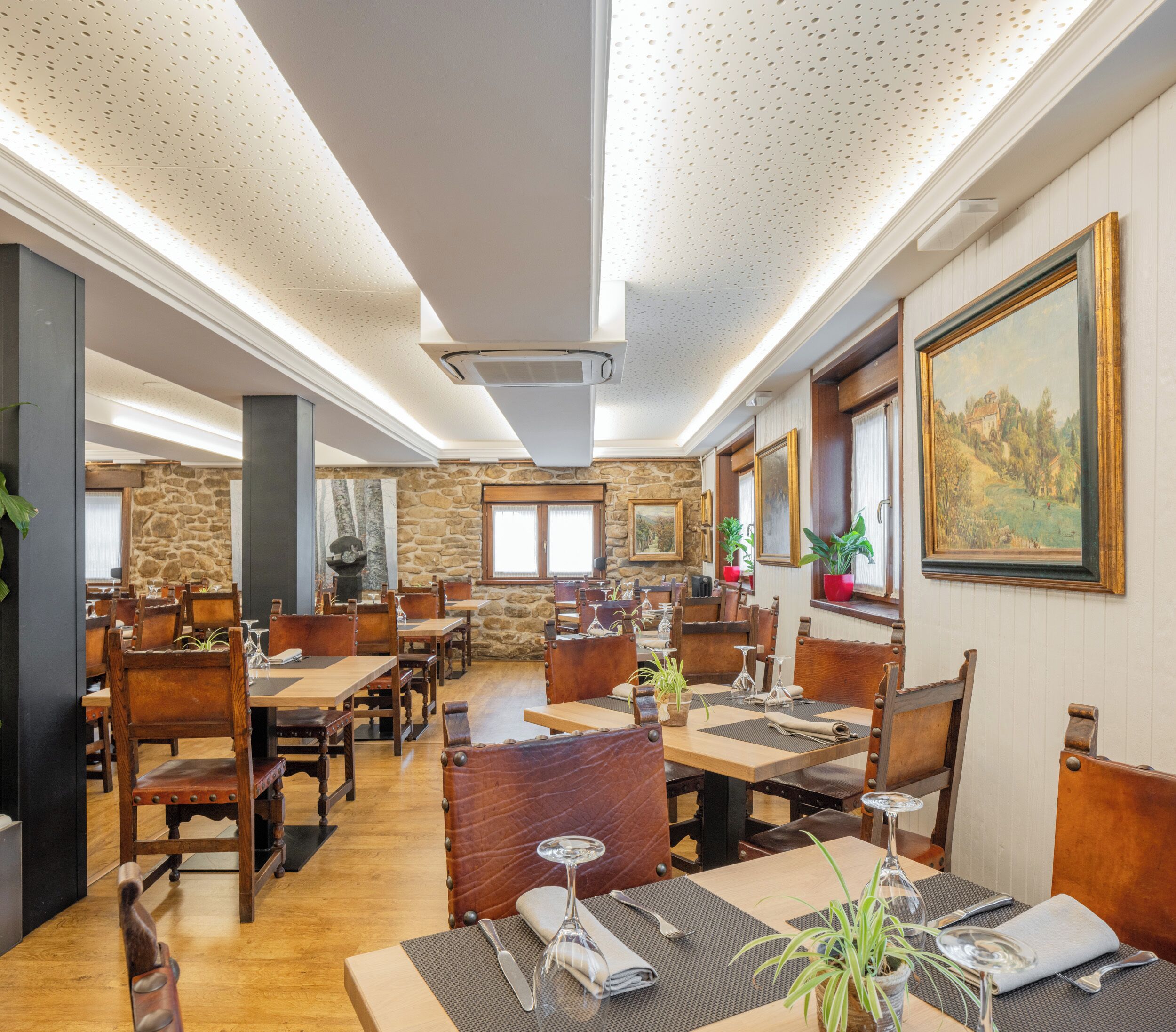 A restaurant with wooden tables and chairs, stone walls, and a painting on the wall.