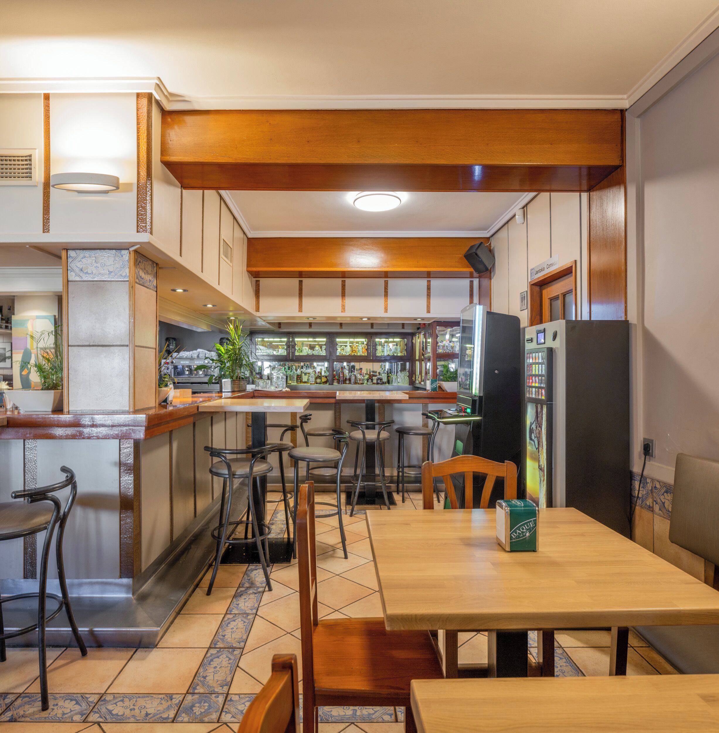 Un restaurante con zona de bar, mobiliario de madera y suelo de baldosas.