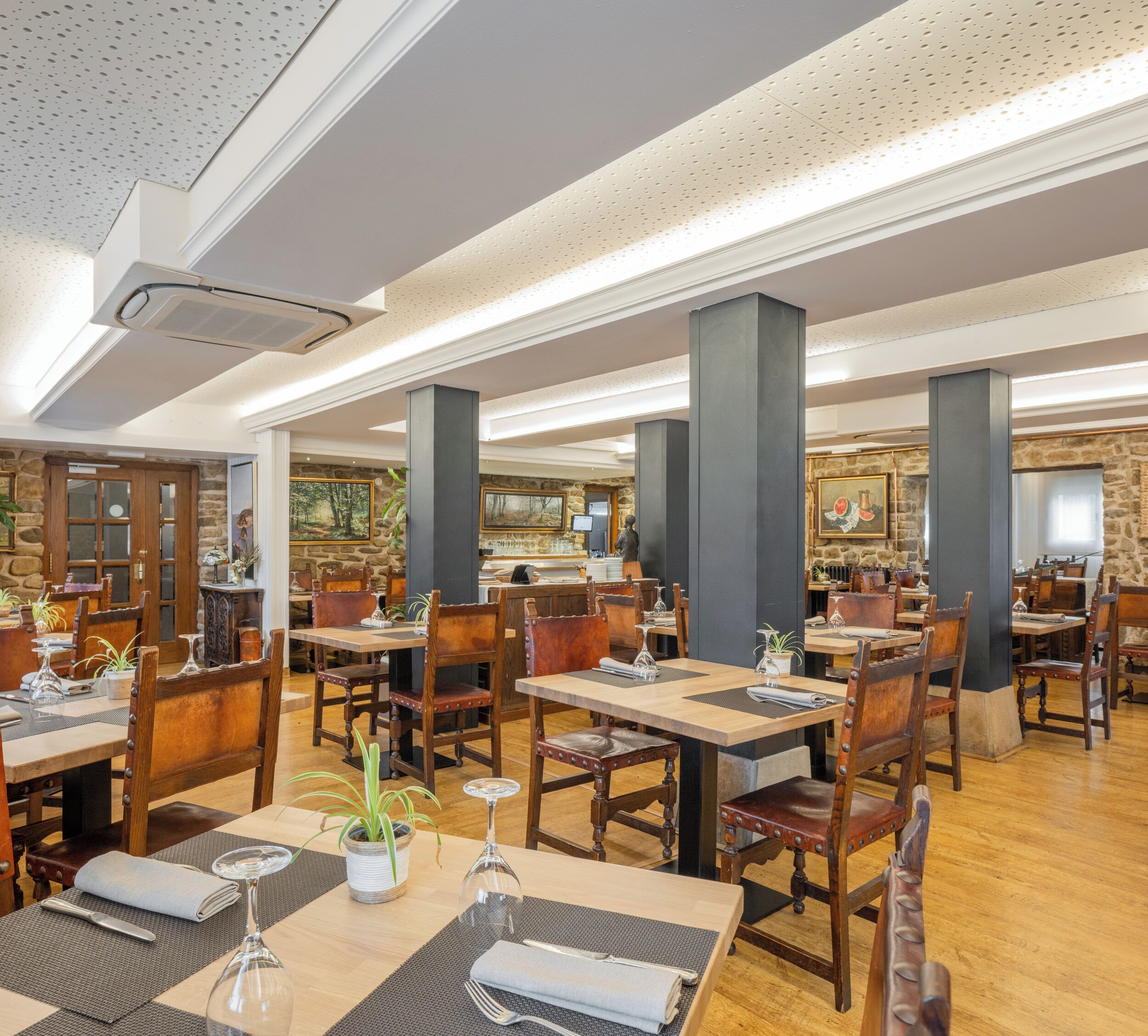 Een ruim restaurant met meerdere eettafels en stoelen, stenen muren en ingelijste kunstwerken aan de wanden.