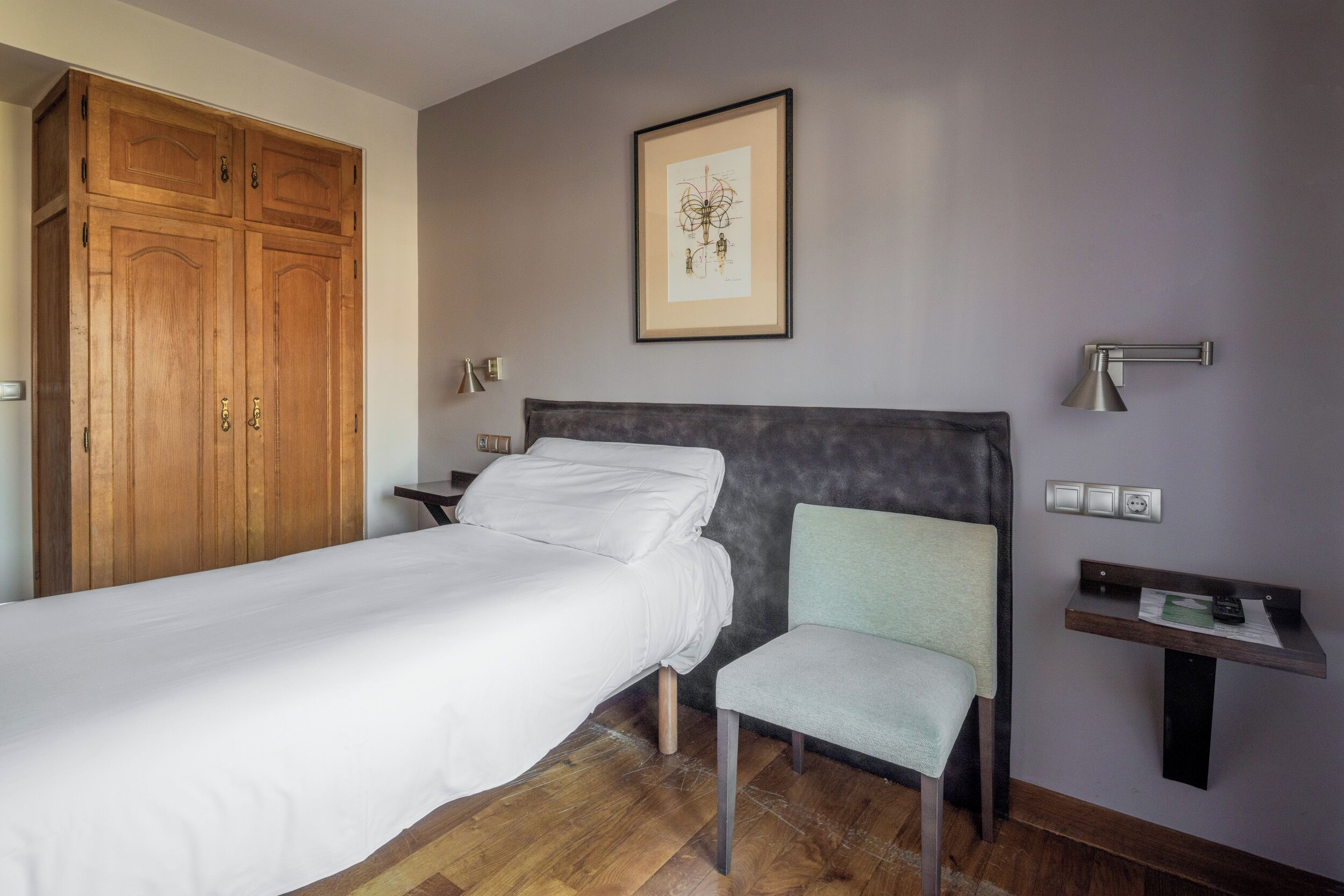 Una camera da letto con un letto, una sedia, un comodino, una scrivania, un quadro incorniciato e un armadio.