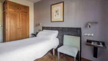 Una camera da letto con un letto, una sedia, un comodino, una scrivania, un quadro incorniciato e un armadio.