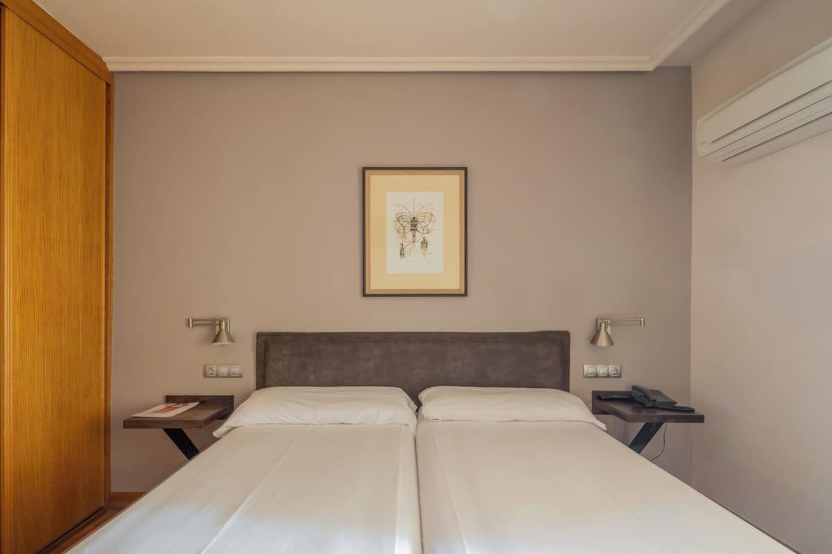 Een hotelkamer met een tweepersoonsbed, een ingelijste afbeelding aan de muur, bedlampen en een houten kledingkast.