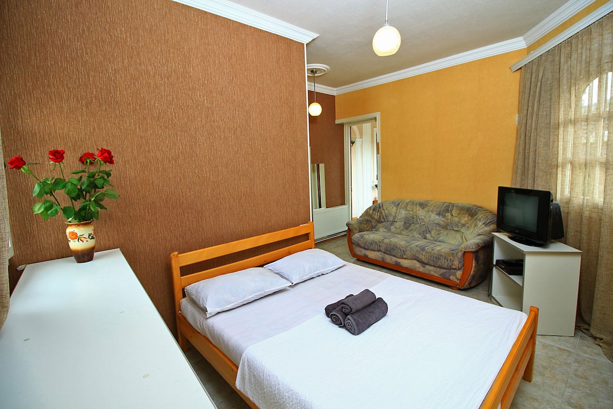 A hotel room with a bed, a sofa, a TV, and a table with a vase of flowers.