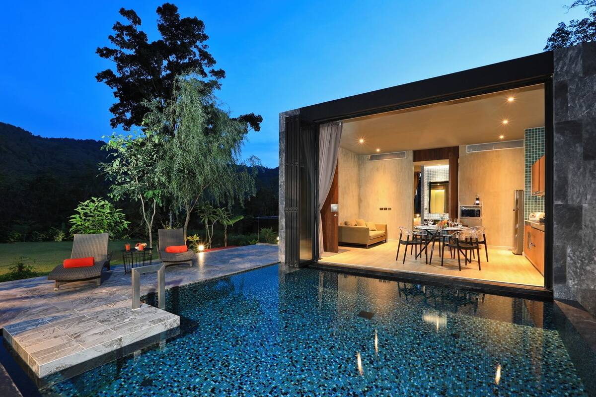 A modern house with an infinity pool, a dining area, and a kitchen visible through large glass doors.