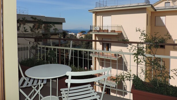 A balcony with a white table and chairs, overlooking a residential area with buildings and a clear sky. - SOGGIORNISORRENTO (Sorrento)
