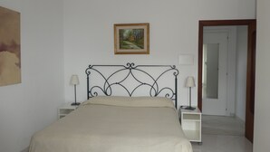 A bedroom with a bed, two bedside tables, a nightstand, a painting on the wall, and a door leading to another room. - SOGGIORNISORRENTO (Sorrento)