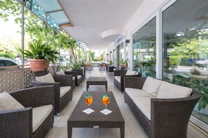 Un espace extérieur aménagé, abrité et doté de mobilier en osier et de plantes en pot.