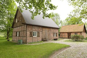 A traditional brick building with a sloped roof, a wooden bench outside, and a cobblestone path leading to it.