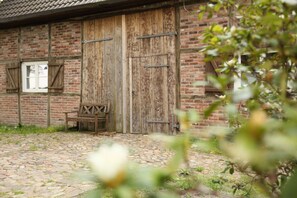 A rustic brick building with wooden doors and shutters, a bench, and a stone-paved courtyard. - Ferienwohnung Ingrid Marie (Stade)