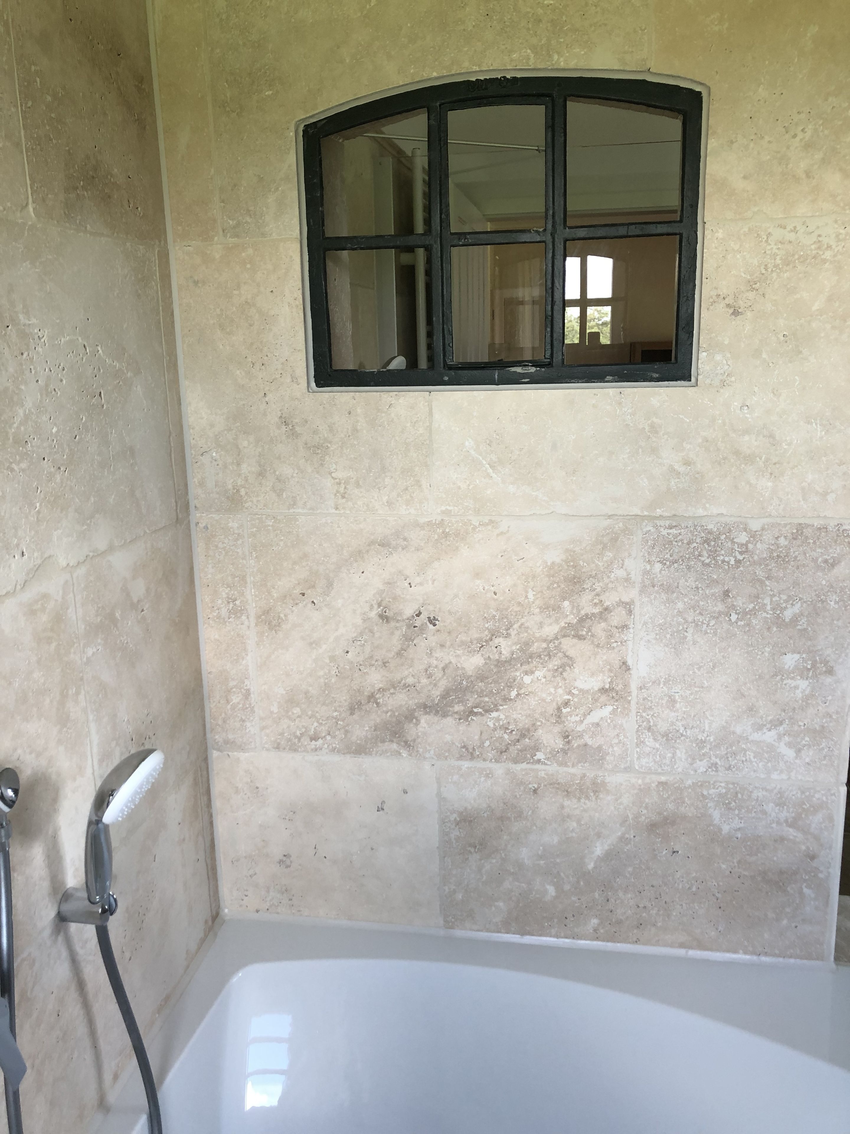 A bathroom with a bathtub, a window with a black frame, and tiled walls.
