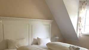 Une chambre à coucher avec un lit blanc, une table de chevet et une lampe.