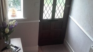 A room with a wooden floor, a window with a metal grid, a door with a decorative design, and a wall-mounted light fixture. - EsJays at Knowles House (Lytham St. Anne's)