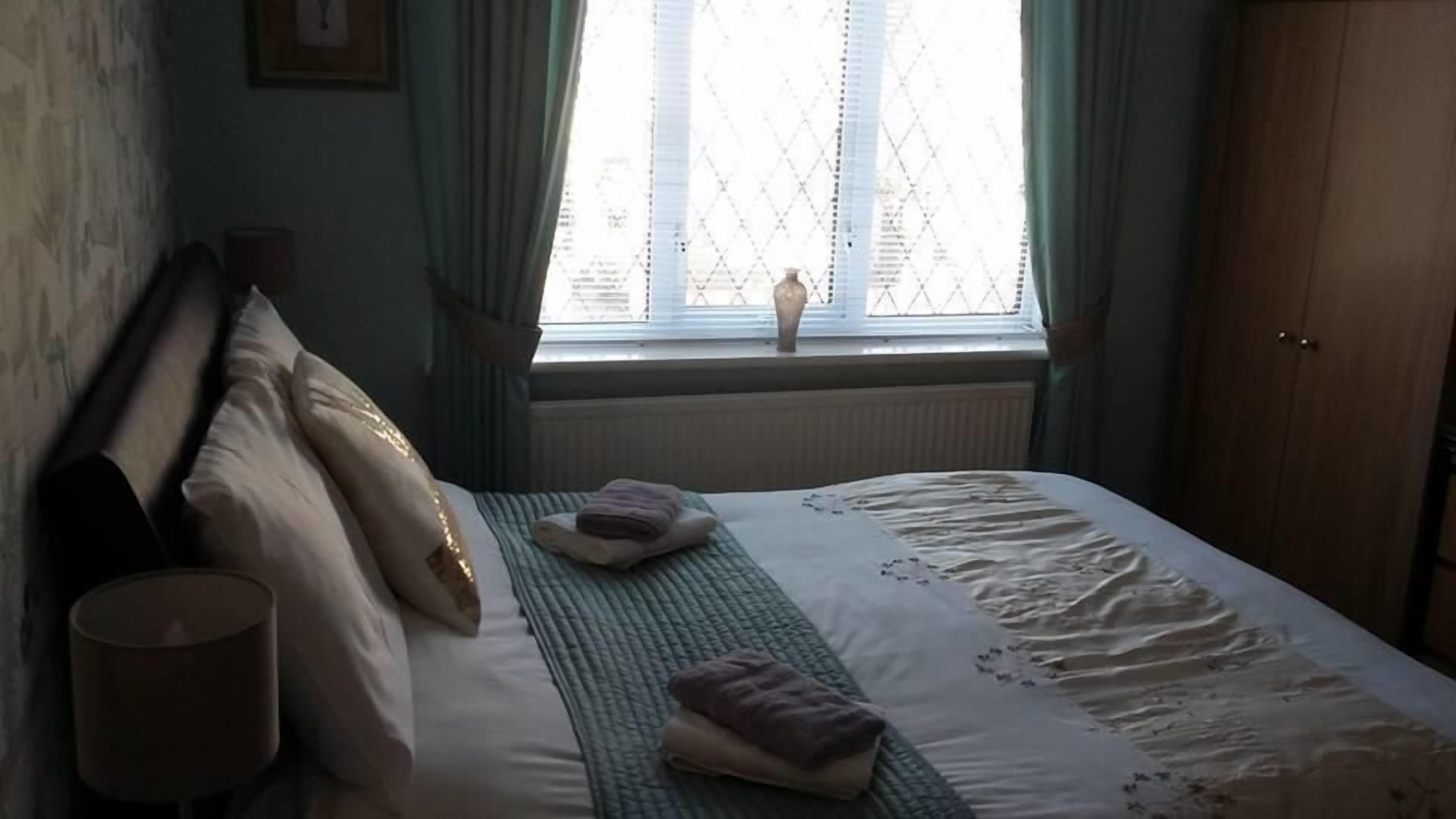 A bedroom with a bed, pillows, a bedside lamp, and a window with curtains.
