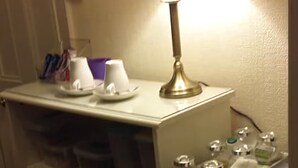 A kitchenette with a lamp, a refrigerator, and shelves with storage containers. - EsJays at Knowles House (Lytham St. Anne's)