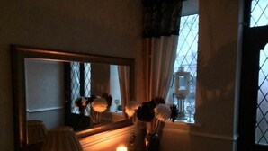A dimly lit room with a mirror, a vase with flowers, a candle, and a window with curtains. - EsJays at Knowles House (Lytham St. Anne's)