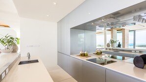 Une cuisine moderne dotée d’un grand îlot central, d’appareils électroménagers en acier inoxydable et offrant une vue sur l’océan.