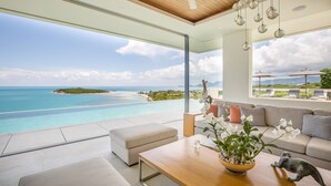 Un salon moderne doté d’une grande baie vitrée donnant sur une plage et l’océan.