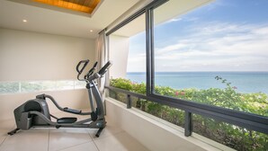 Une chambre moderne dotée d’une grande fenêtre donnant sur la mer, d’un tapis de course et d’un balcon agrémenté de plantes.