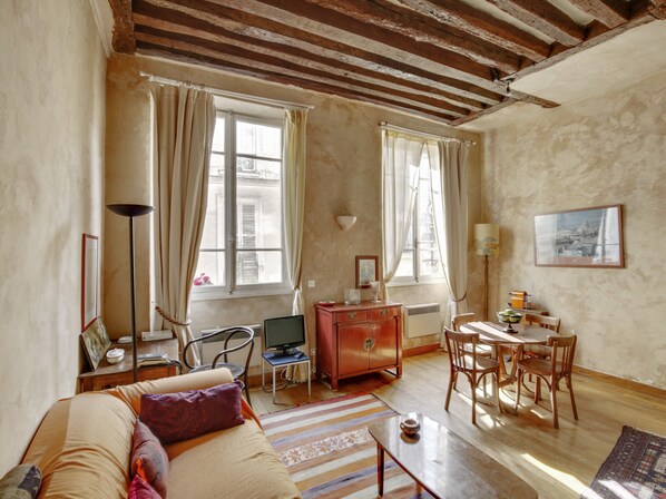 A cozy living room with a sofa, a coffee table, a TV, a dining table with chairs, and a fireplace.